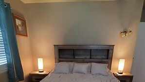 Un dormitorio con una cama grande, dos mesitas de noche con lámparas, un cabecero de madera y un cuadro enmarcado en la pared.