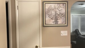 Un pasillo con una puerta blanca, un cuadro enmarcado en la pared y un panel de pared oscuro.