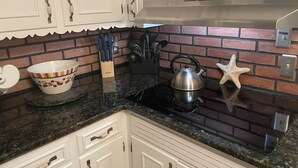 Una cocina con armarios blancos, salpicadero de ladrillo, una tetera y un bol en la encimera.
