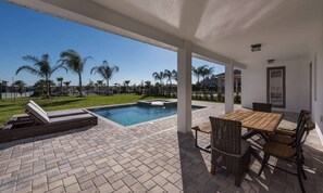 A covered outdoor area with a pool, lounge chairs, and a dining table. - Rent this Luxury 5 Star Villa on Encore Resort at Reunion, Orlando Villa 5456 (Orlando)