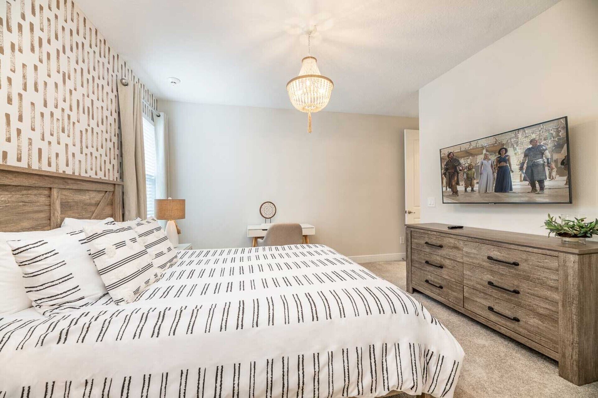 A bedroom with a bed, bedside table, lamp, dresser, and a painting on the wall.