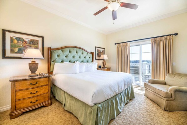 A hotel room with a large bed, a wooden dresser, two bedside lamps, a ceiling fan, and a balcony with curtains.