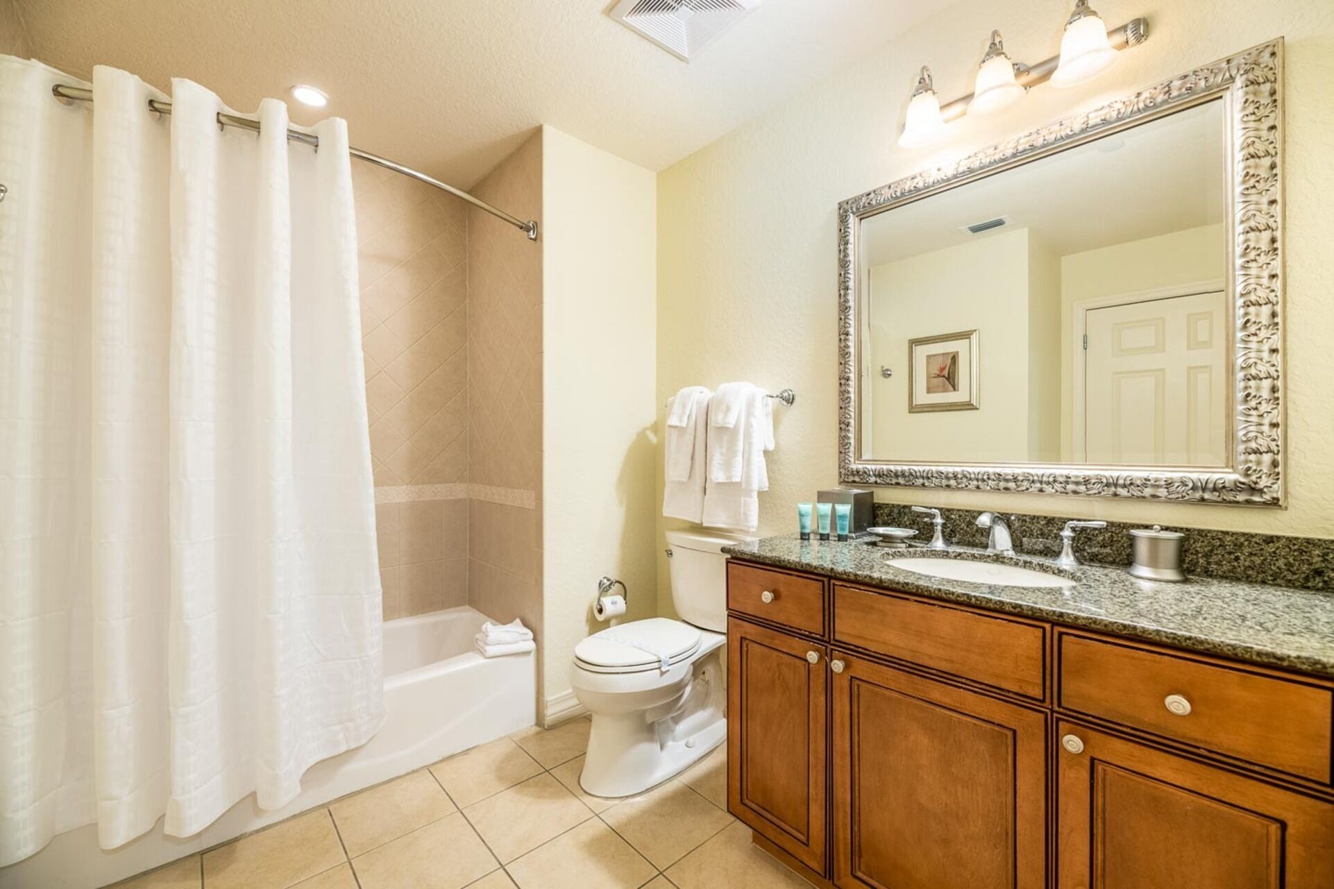 A bathroom with a shower, toilet, vanity with sink, and a large mirror.