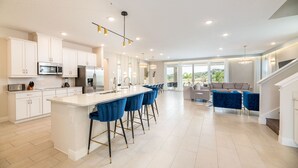 Une cuisine moderne avec des meubles blancs, des appareils en acier inoxydable et un îlot central doté de tabourets de bar bleus.