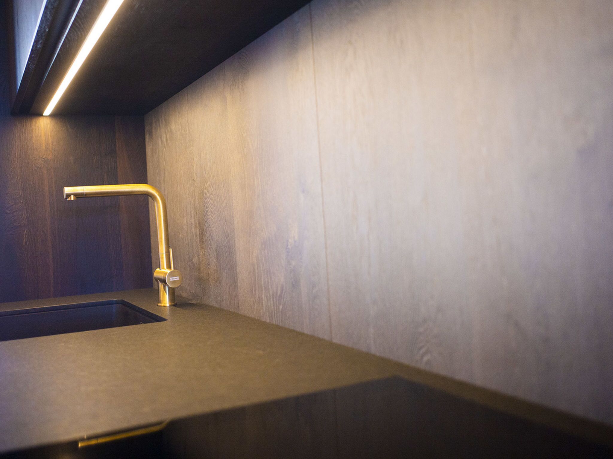 Un baño moderno con un lavamanos individual, un grifo curvo y una tira de luz sobre el espejo.