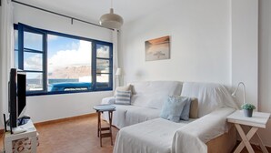 Una habitación con una cama, una mesita, un televisor y una ventana con vista al mar.