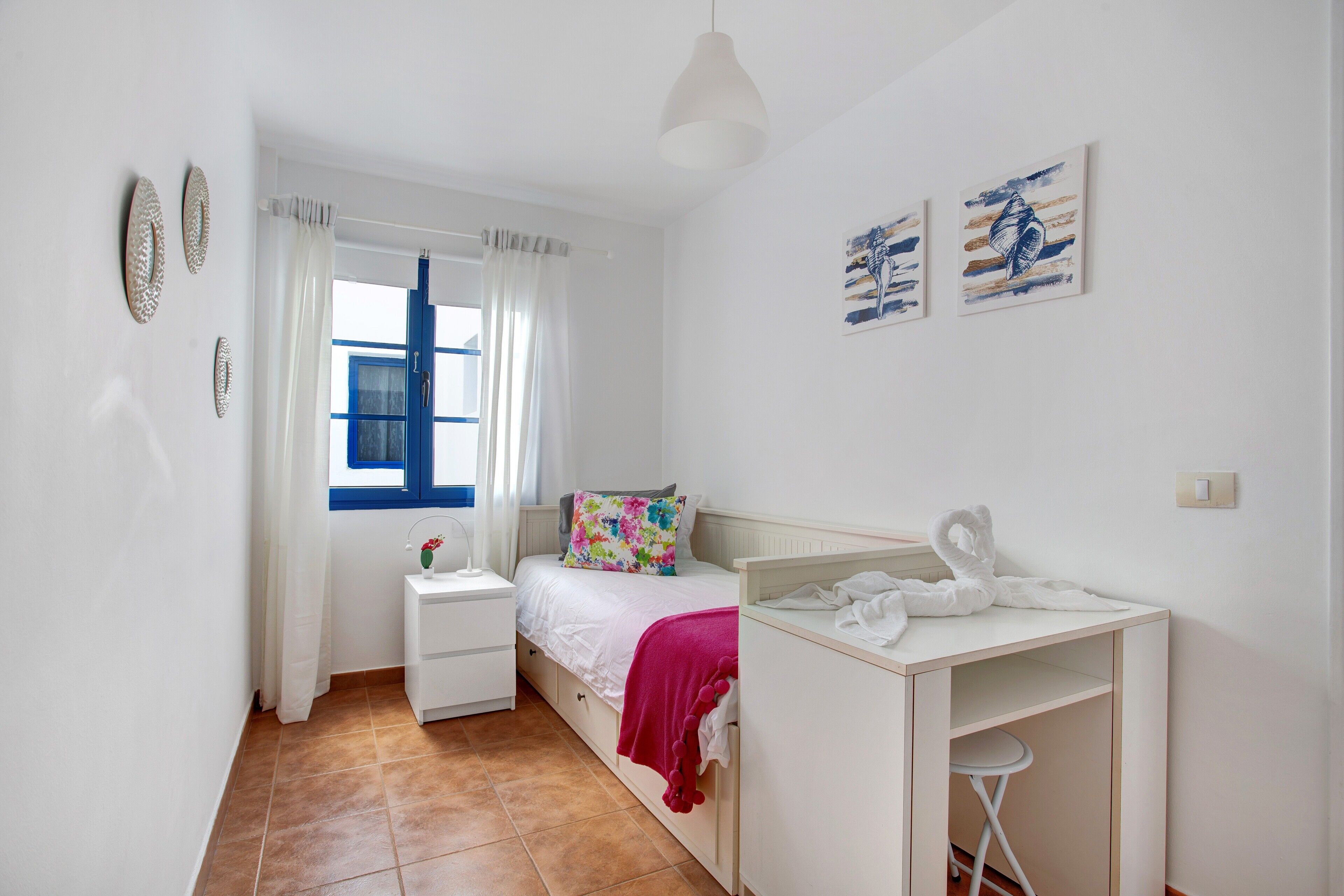 Ein Schlafzimmer mit Bett, Schreibtisch, Stuhl, einem Fenster mit Vorhängen und Wandbildern.