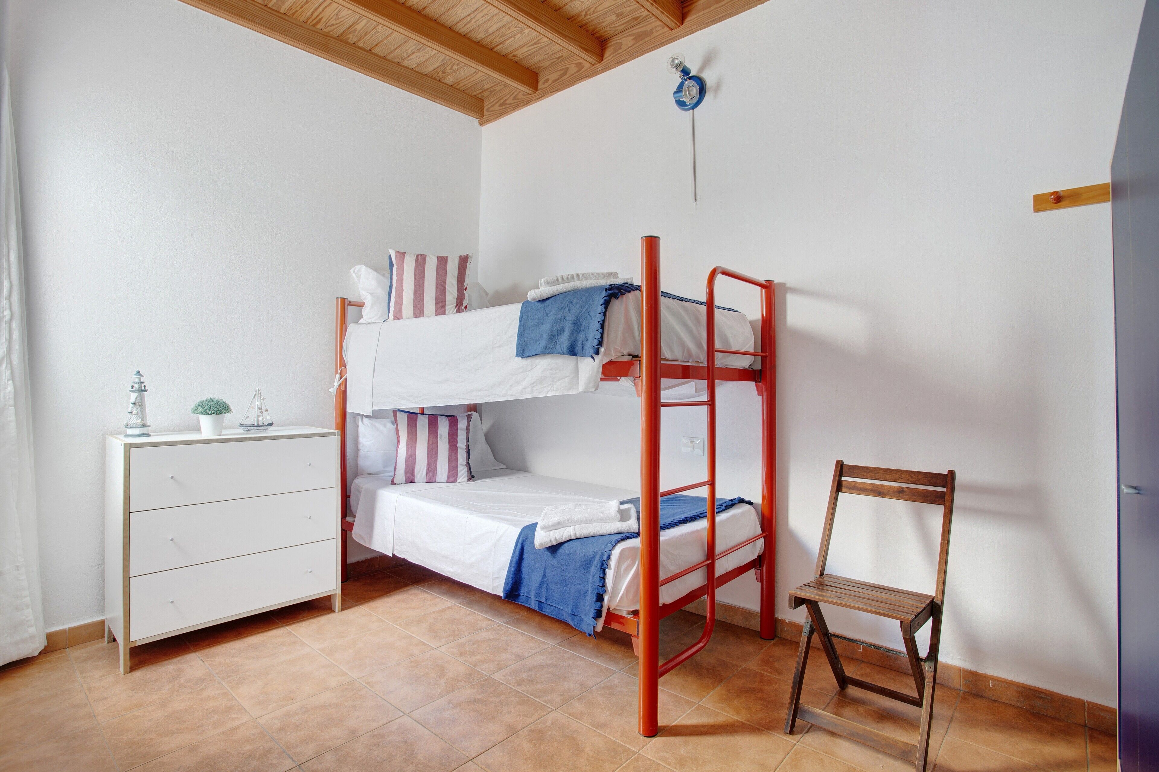 Een stapelbed met bureau en stoel, een klein dressoir en een wandlamp.
