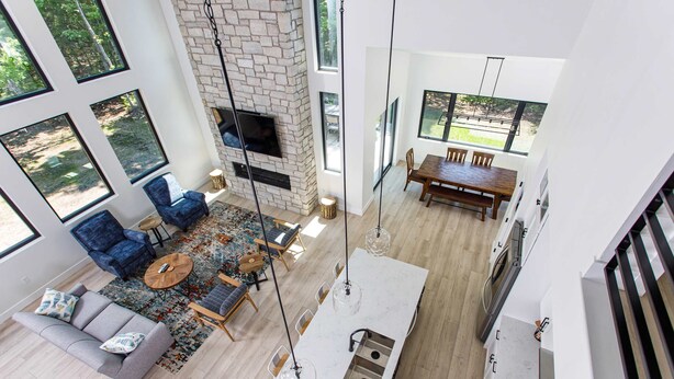 A modern living room with a fireplace, large windows, a dining area, and a kitchen island. - Expansive Modern Loft House Sleeps 12 (Egg Harbor)