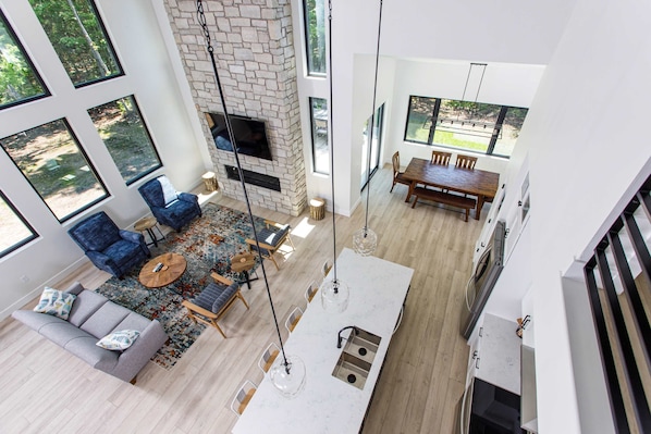 A modern living room with a fireplace, large windows, a dining area, and a kitchen island.