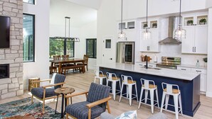 A modern kitchen with white cabinets, a central island, bar stools, and pendant lighting. - Expansive Modern Loft House Sleeps 12 (Egg Harbor)
