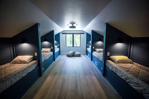 Une pièce avec trois lits superposés, une grande fenêtre et un projecteur au plafond.