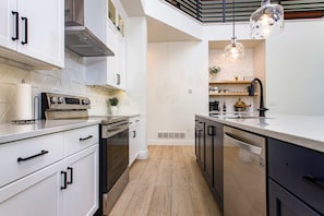 A modern kitchen with white cabinetry, stainless steel appliances, and a wooden floor.