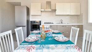 A modern kitchen with white cabinets, a stainless steel refrigerator, and a dining area with a table set for four.