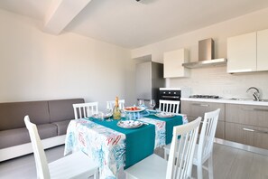 A modern kitchen with white cabinets, a stainless steel range hood, and a dining area with a teal tablecloth.