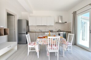 Une cuisine moderne avec des meubles blancs, un réfrigérateur en acier inoxydable et un coin repas agrémenté d’une nappe colorée.