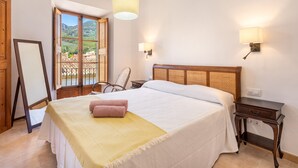 Ein Schlafzimmer mit Bett, einem Holznachttisch, einem Sessel, einem Fenster mit Blick und einer Pendelleuchte.