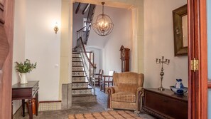 Un escalier avec des marches décorées, une chaise en bois, un chandelier et une horloge murale.