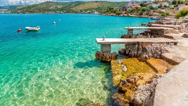 Un paysage côtier avec une eau turquoise et limpide, des affleurements rocheux et quelques bateaux.