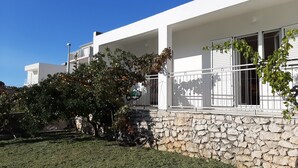 Un bâtiment moderne, de couleur blanche, avec une fondation en pierres apparentes, un porche couvert et un arbre fruitier.
