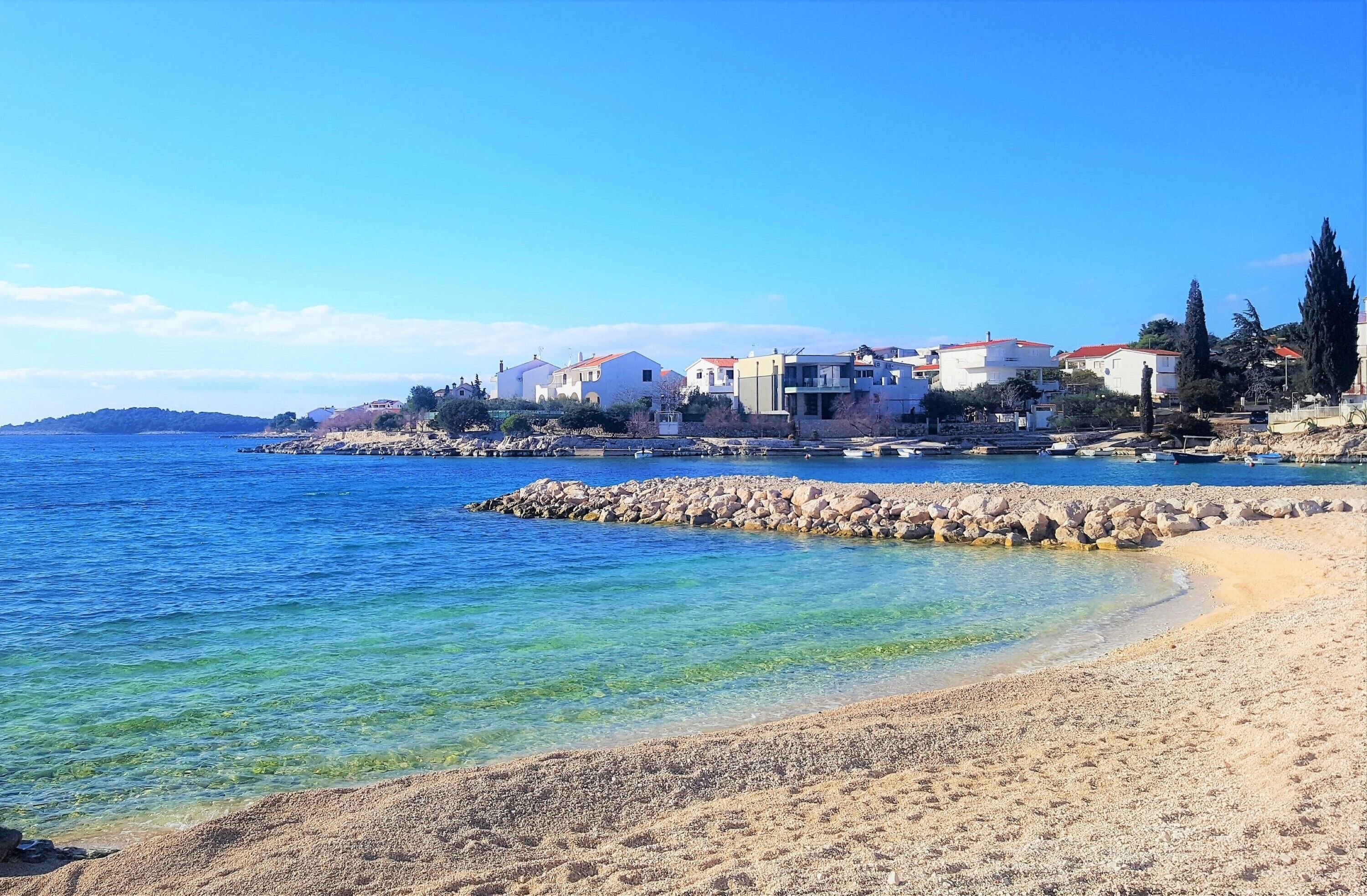 Eine Küstenstadt mit Gebäuden entlang der Uferlinie, klarem, blauem Wasser und einem Sandstrand.