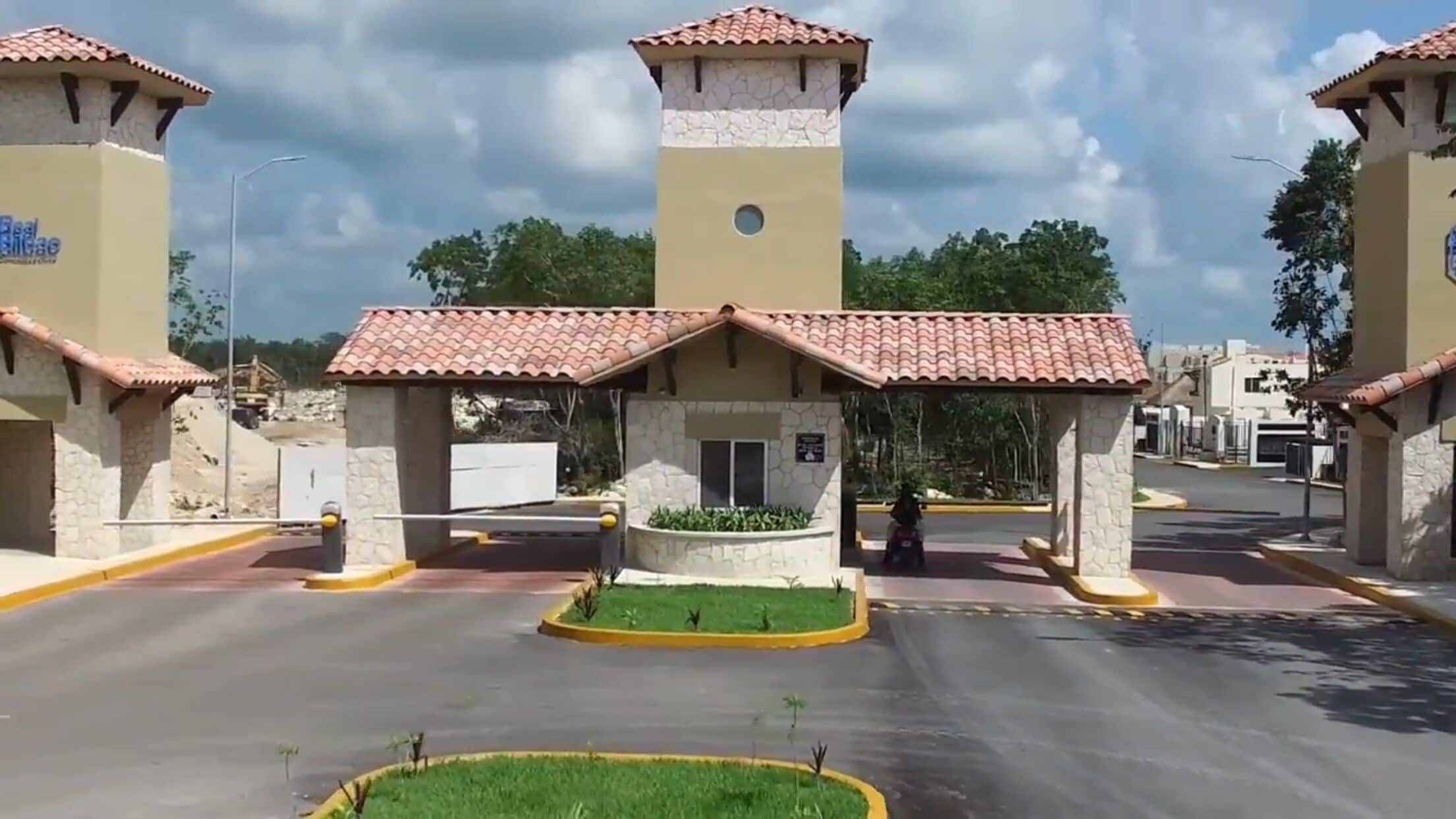 A gated entrance with a central tower and two smaller towers, surrounded by a paved area with a circular garden.