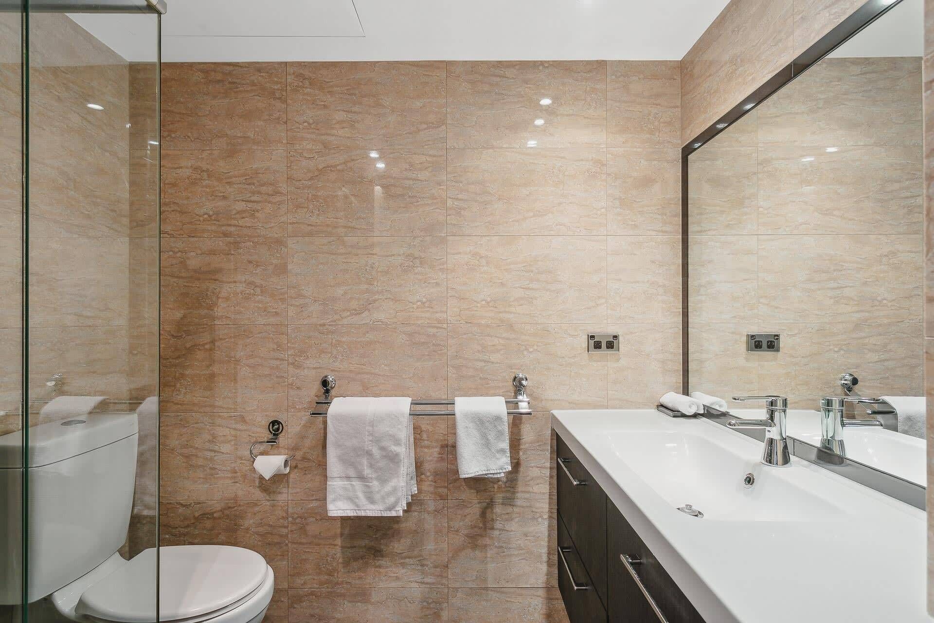 A modern bathroom with a glass shower enclosure, a toilet, a sink, and a large mirror.