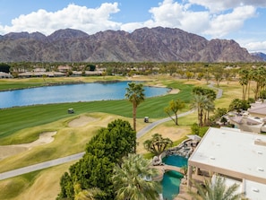A golf course with a lake, palm trees, and mountains in the background.