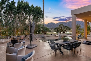 An outdoor patio with a stone fire pit, seating area, and a view of a golf course and mountains.