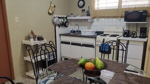 Una cocina compacta con armarios blancos, estufa, microondas y un pequeño comedor con una mesa para dos.