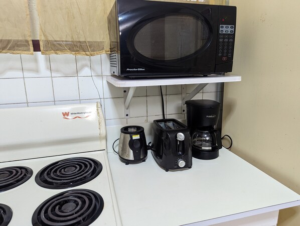 A kitchen with a white stove, a black Proctor Silex microwave, a black coffee maker, and a toaster on a white countertop.