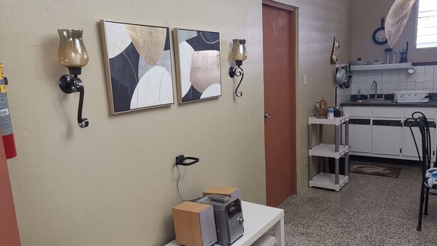 Cocina con armarios blancos, un lavamanos y una encimera. Hay dos lámparas fijadas a la pared y una puerta.