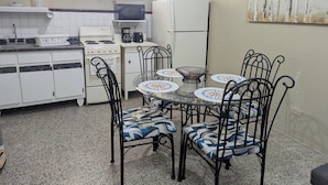 Cocina compacta con armarios blancos, estufa, microondas y refrigerador. Hay una mesa de comedor con sillas y un cuadro decorativo en la pared.