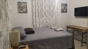 Un dormitorio con cama, una mesa, lámpara, televisor y dos cuadros en la pared.