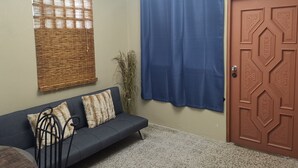 Un salón con un sofá oscuro, un tapiz decorativo, una cortina azul, una puerta con intrincados grabados y una araña.