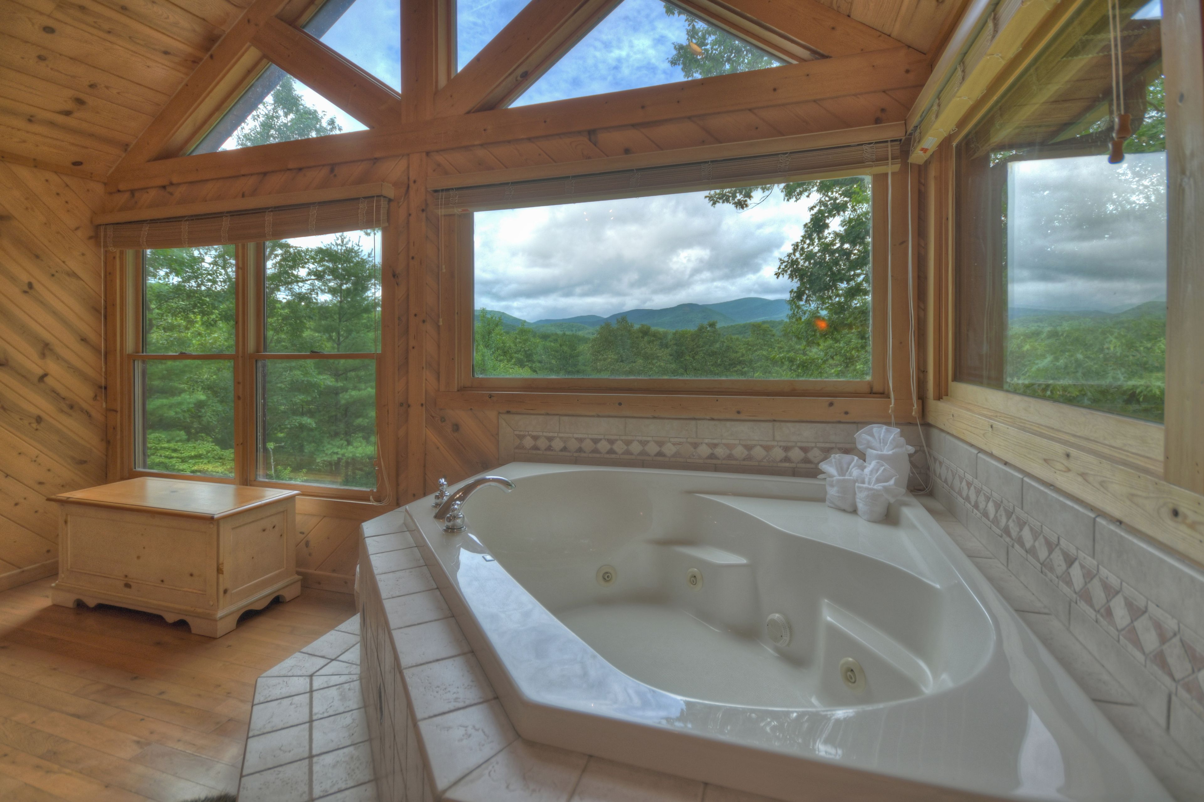 Ein Badezimmer einer Holzhütte mit einer großen Badewanne, Holzwänden und großen Fenstern mit Blick auf den Wald.