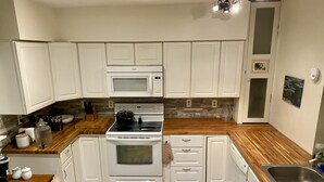 A modern kitchen with white cabinets, a built-in microwave, a stove, and a wooden countertop.