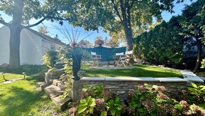 A well-maintained garden with a stone wall, a seating area with chairs, and a blue fence in the background.