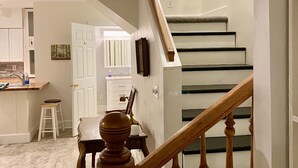 A staircase with wooden balusters and a handrail, leading to a landing with a white door and a small table with a chair.