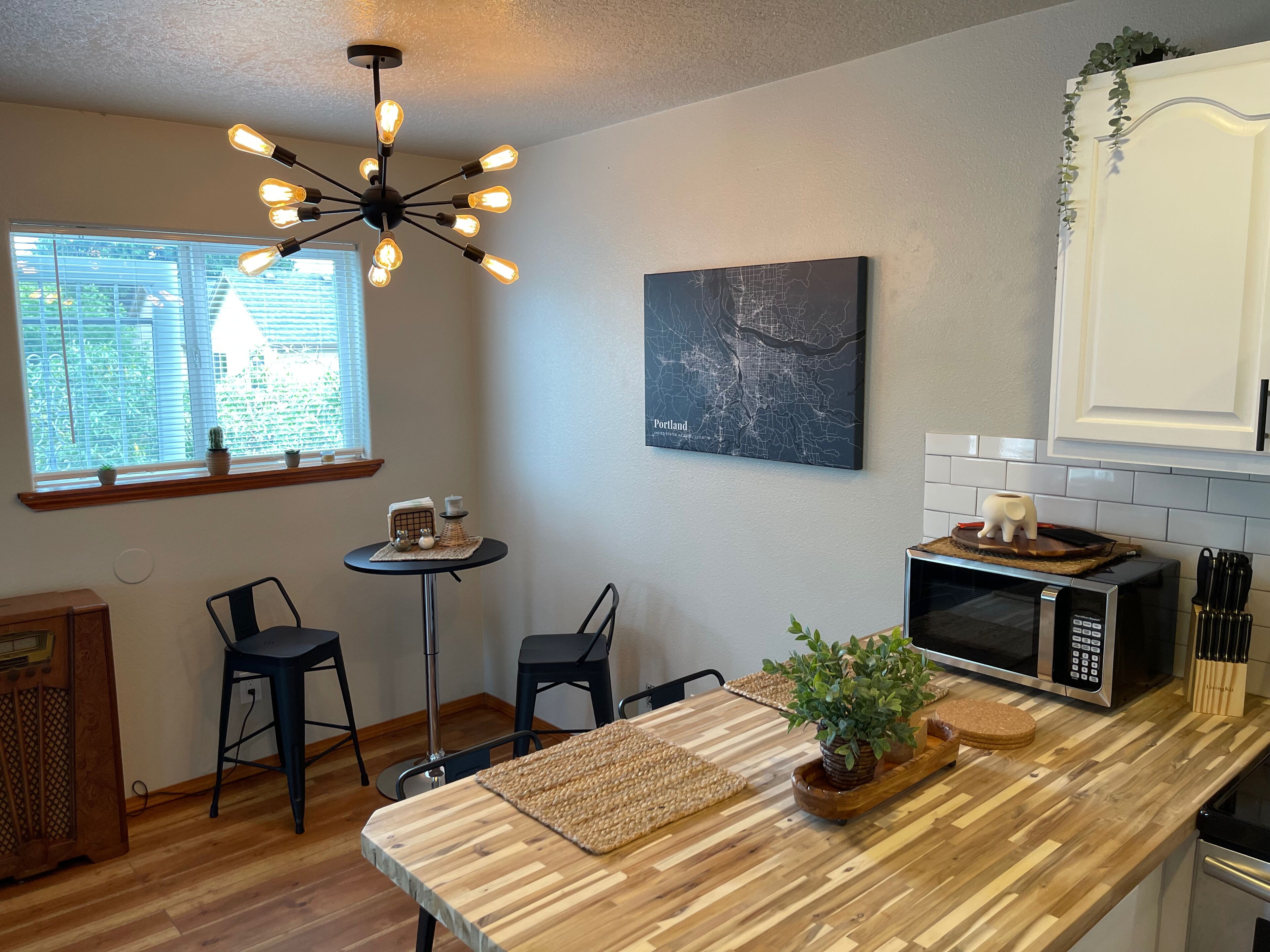 A kitchen with a wooden countertop, a microwave, a coffee machine, and a dining area with two chairs and a small table.