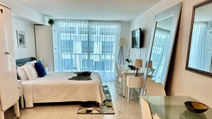A hotel room with a bed, a desk, a chair, a TV, and a large window with curtains. - Mesmerizing Studio Brickell +Free Parking + Gym+Pool (Miami)