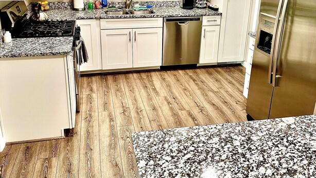A modern kitchen with white cabinets, a granite countertop, a stainless steel refrigerator, and a dishwasher.