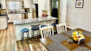 A modern kitchen with white cabinets, granite countertops, and a dining area with a wooden table and bar stools.
