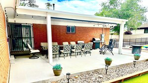 A covered patio with outdoor seating, a barbecue grill, and a potted plant.