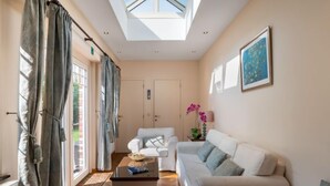 A spacious living room with a high ceiling, a skylight, and a large window. There is a white sofa, a coffee table, and a potted orchid. - Jasmine by Interhome (Mol)