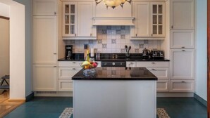 A kitchen with white cabinets, a black countertop, and a central island with fruit. - Jasmine by Interhome (Mol)