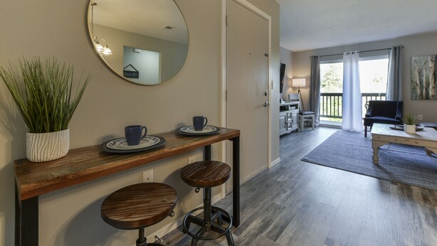 A modern living area with a wooden console table, two stools, a round mirror, and a potted plant. - Mercy's Hideaway - Open Pool! Relaxing & Chic! Prime Location w/ Natural Views! (Branson)
