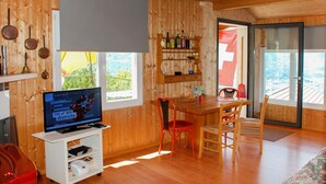 Ein Holzinnenraum mit Fernseher, der Nachrichten zeigt, einem Essbereich und Blick durch eine Glastür.
