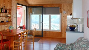 Ein Holzinnenraum mit Essbereich, einer Couch, einer Küche mit Spüle und Blick durch eine Glastür.