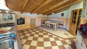 A kitchen with a checkered floor, wooden ceiling beams, a dining area with a table and chairs, and a red exercise machine.